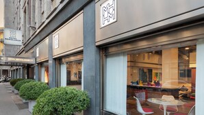 A hotel exterior with a modern facade, large windows, and outdoor seating area. - Hotel Mediolanum (Milan)
