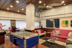 A modern living room with a foosball table, a sofa, a coffee table, and a large abstract painting on the wall.