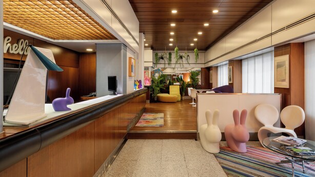 A modern hotel lobby with wooden paneling, a reception desk, seating areas, and decorative elements like bunny-shaped chairs. - Hotel Mediolanum (Milan)