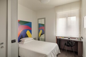 A hotel room with a bed, desk, chair, and a window with blinds.