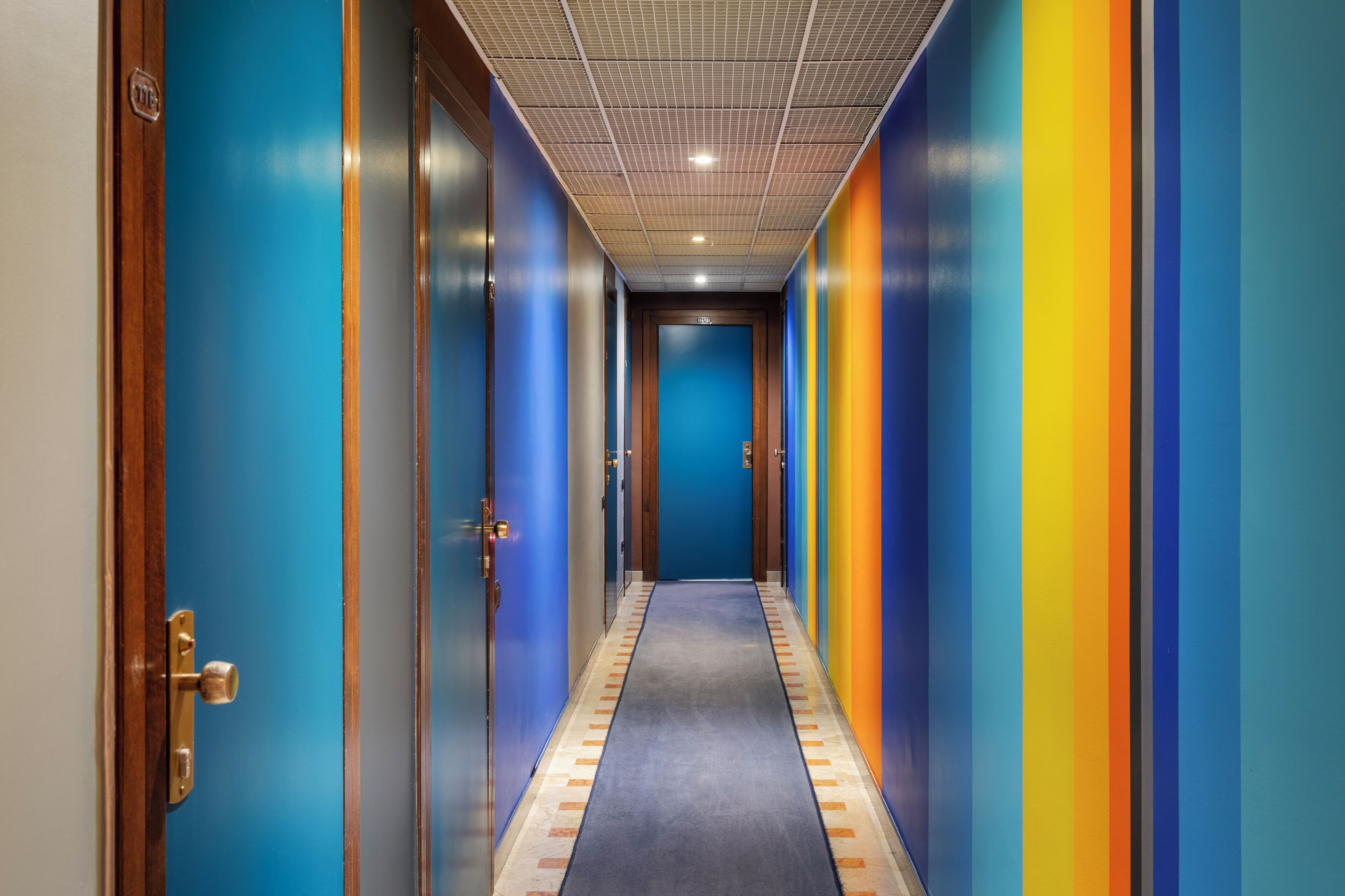 A hallway with doors on both sides, a carpeted floor, and a ceiling with recessed lighting.