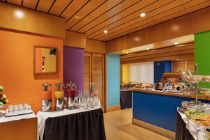 Un buffet per la colazione con diversi cibi e bevande, un soffitto in legno e un'allegra decorazione murale.