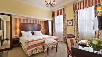 Quarto de hotel com uma cama grande, uma escrivaninha com cadeira, uma televisão e um espelho.