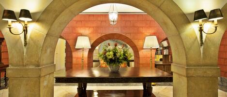 Un vestíbulo con piso de mármol, una mesa central con un jarrón de flores y dos lámparas a cada lado.