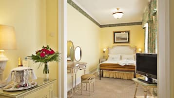 Une chambre d’hôtel comprenant un lit, une télévision, un bureau avec une lampe, une coiffeuse avec un miroir et un vase avec des fleurs.