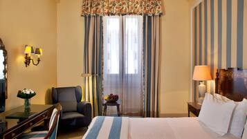 Habitación de hotel con cama, escritorio con lámpara, una silla, una mesita con frutero y cortinas.