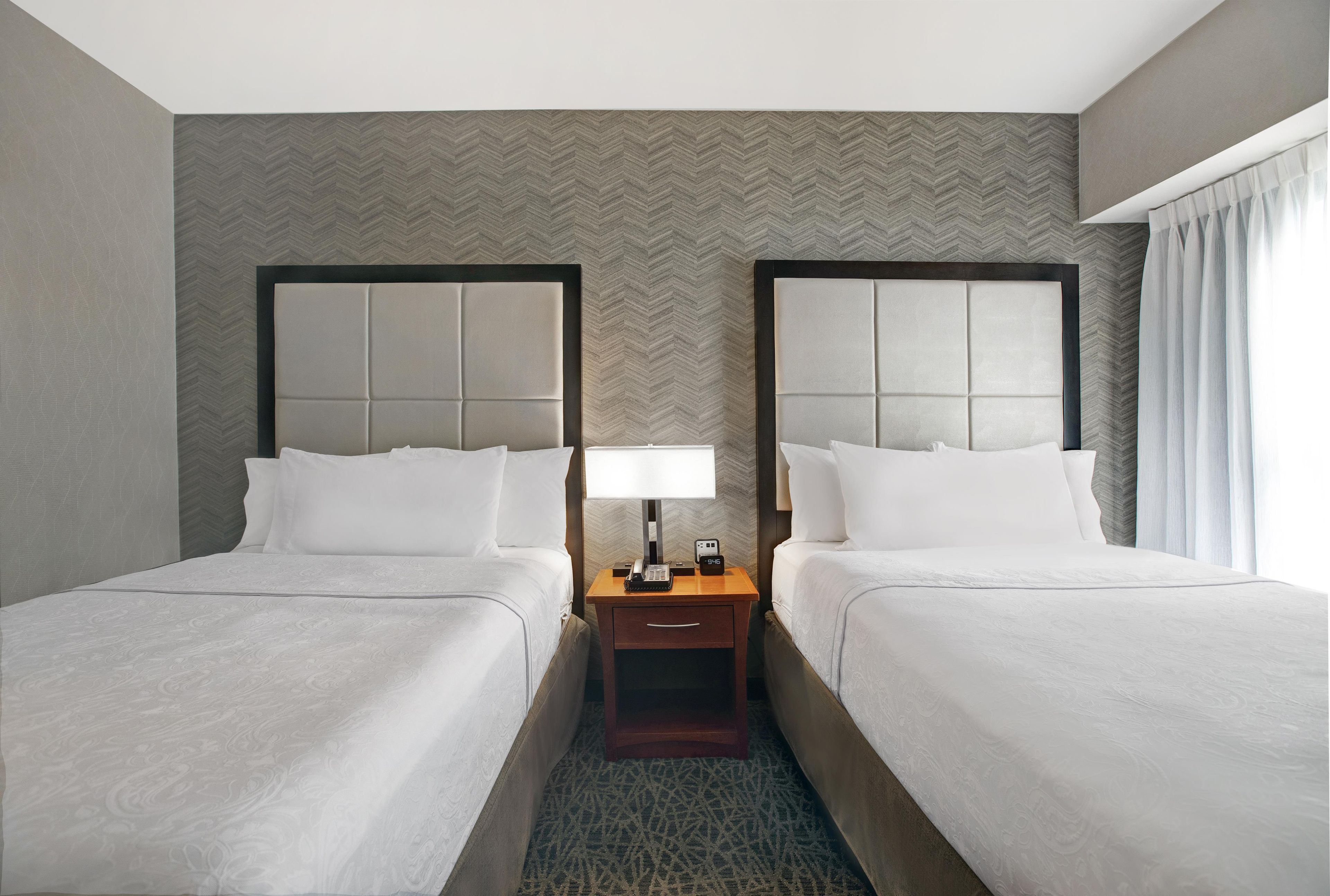 Une chambre d’hôtel avec deux lits, une table de chevet avec une lampe et un mur orné d’un motif en chevrons.