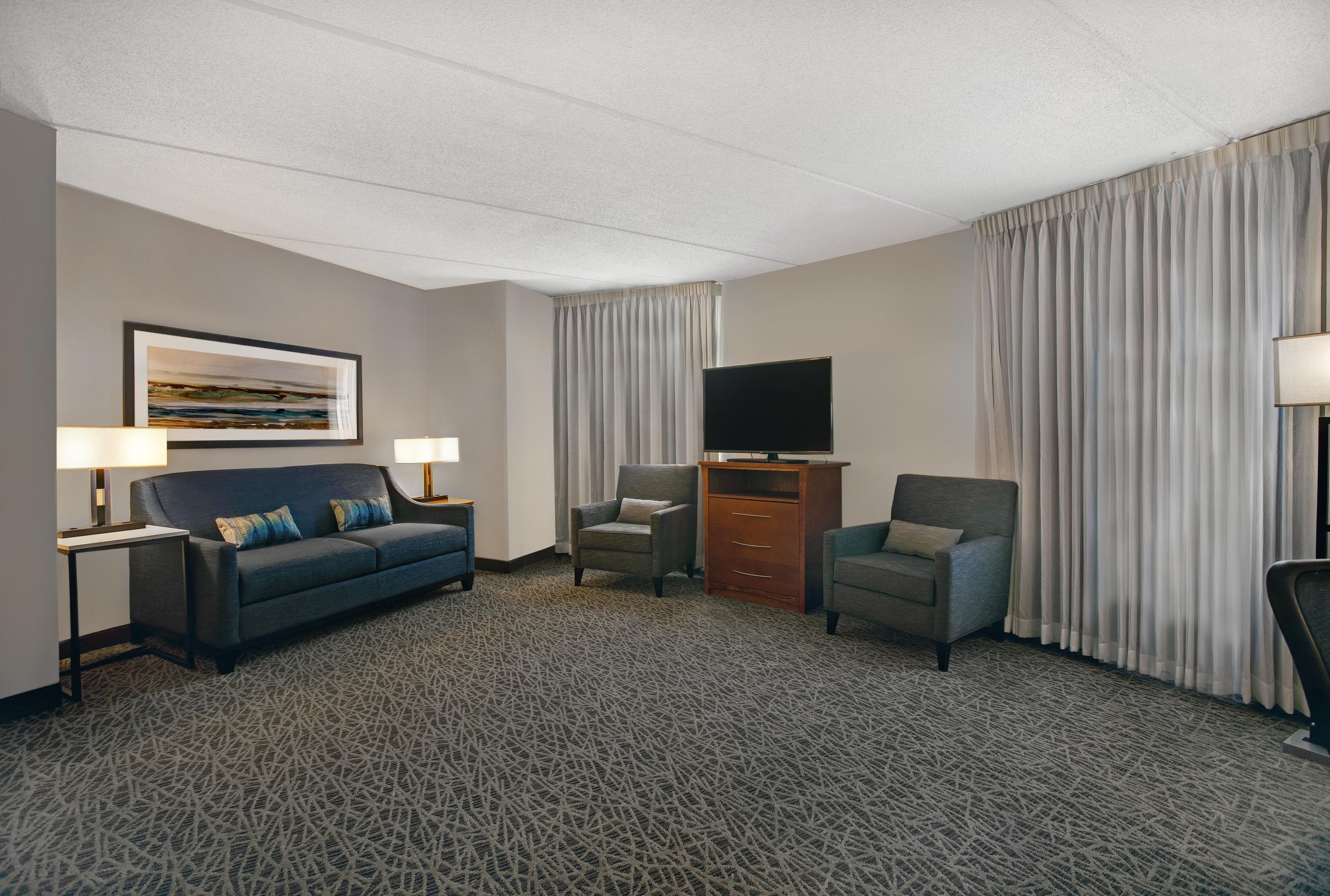 A hotel room with a sofa, two armchairs, a flat-screen TV, a wooden cabinet, and a patterned carpet.