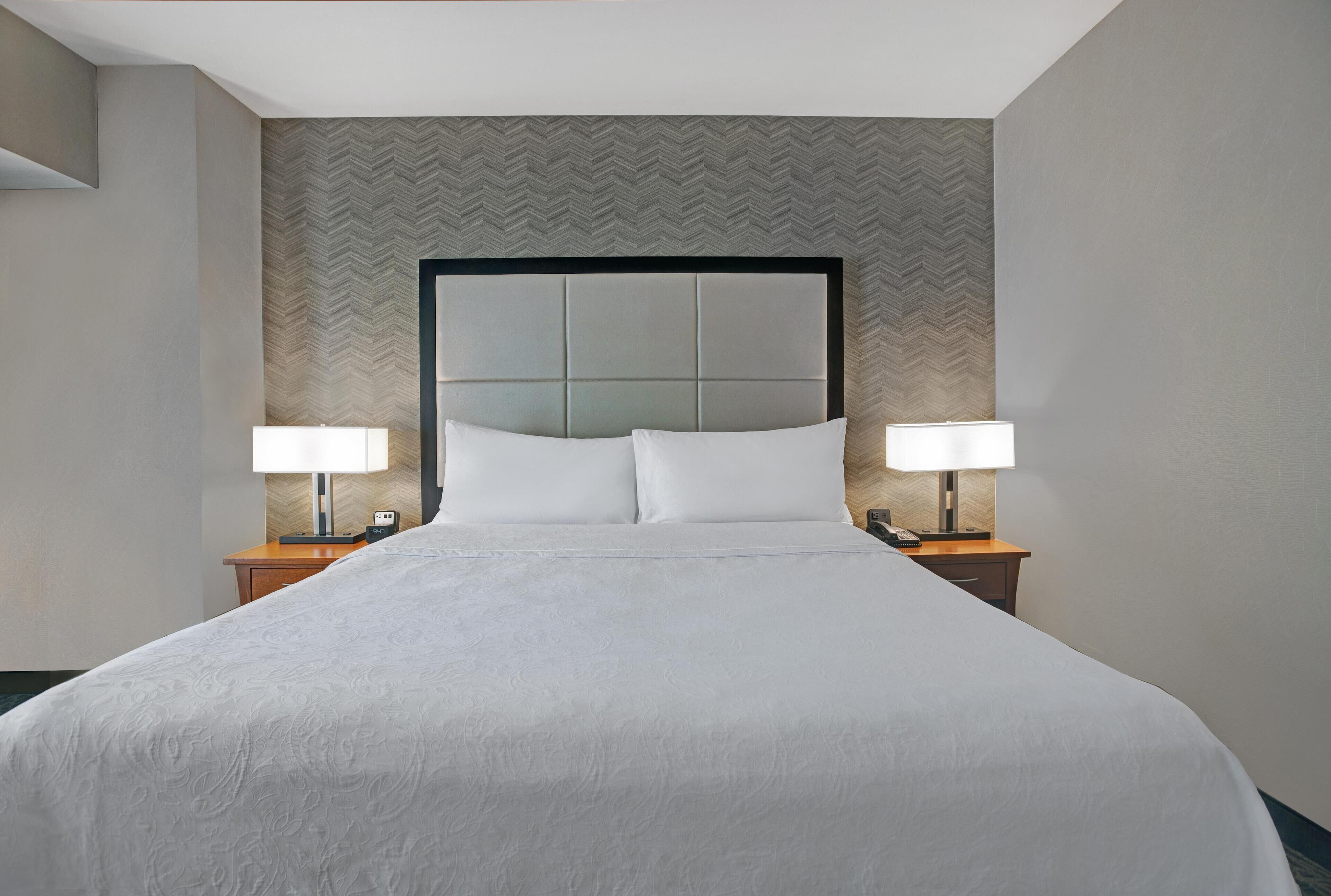 Habitación de hotel con una cama grande, dos mesitas de noche con lámparas y un papel tapiz de diseño en patrón espiga.