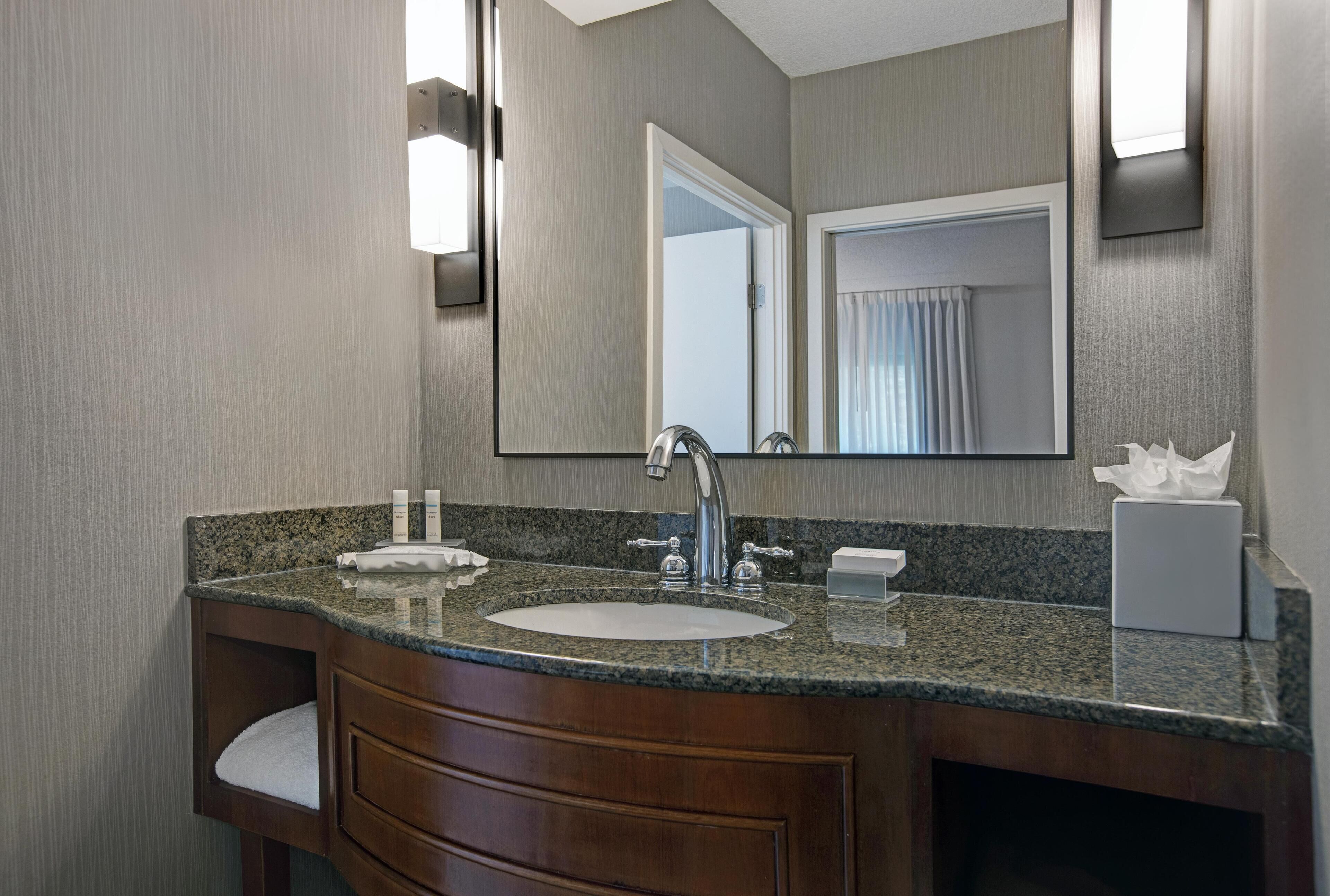 A bathroom with a granite countertop sink, wooden vanity, and a large mirror.