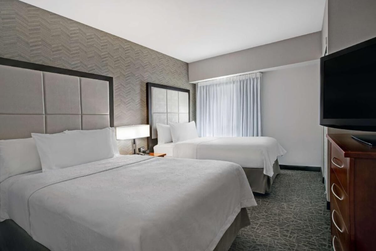 Een hotelkamer met twee bedden, een flatscreen televisie, een dressoir en een raam met gordijnen.