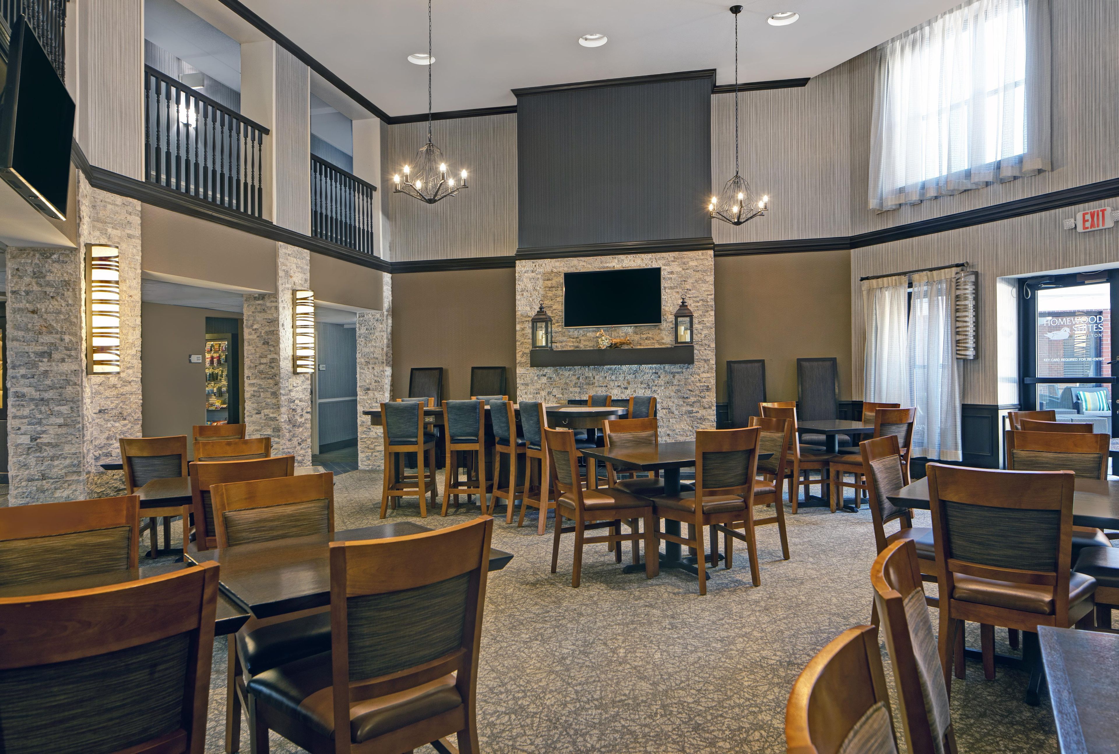 A spacious dining area with multiple tables and chairs, a stone accent wall, and a flat-screen TV mounted above a fireplace.