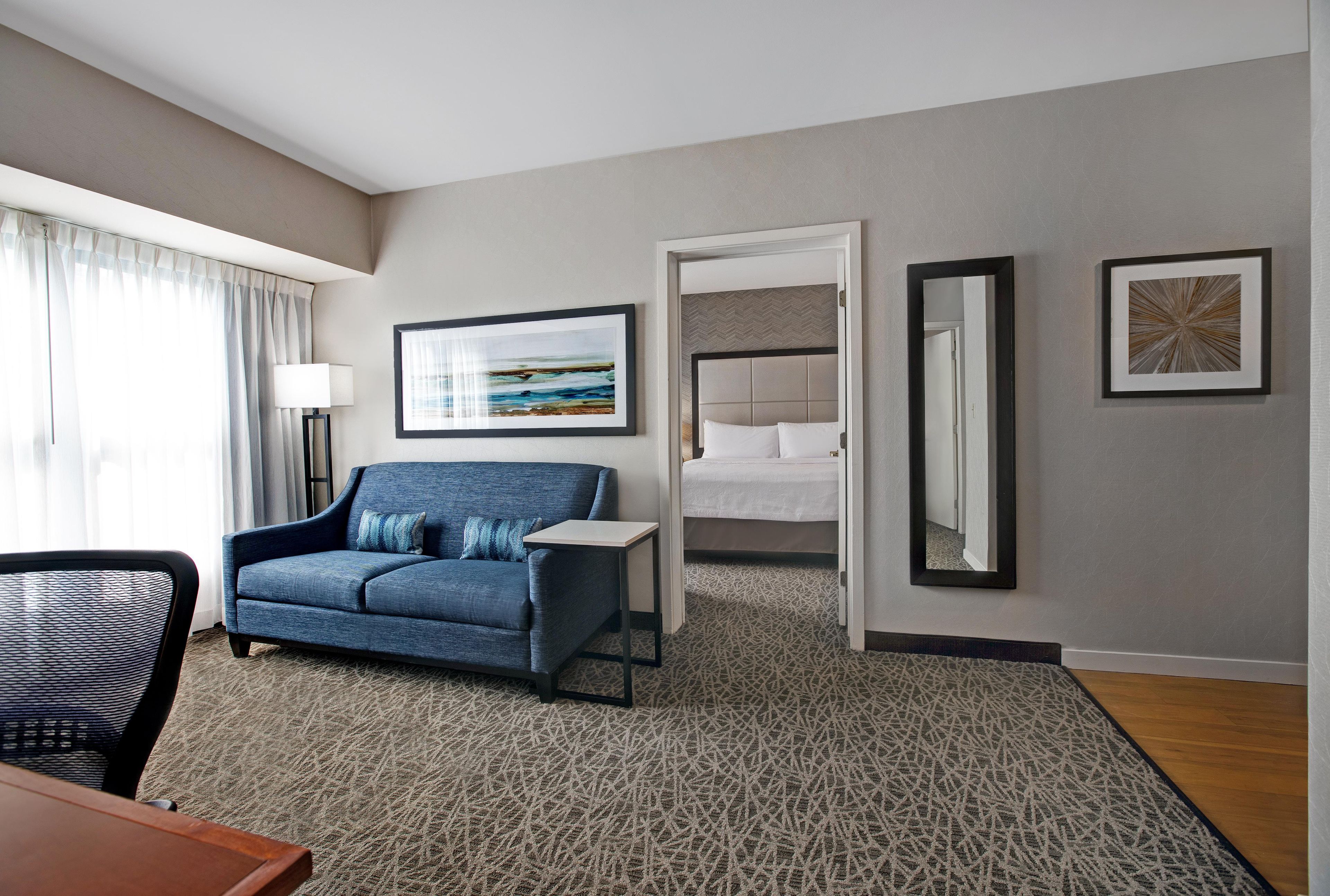 A hotel room with a sofa, a bed, a desk, and a mirror.