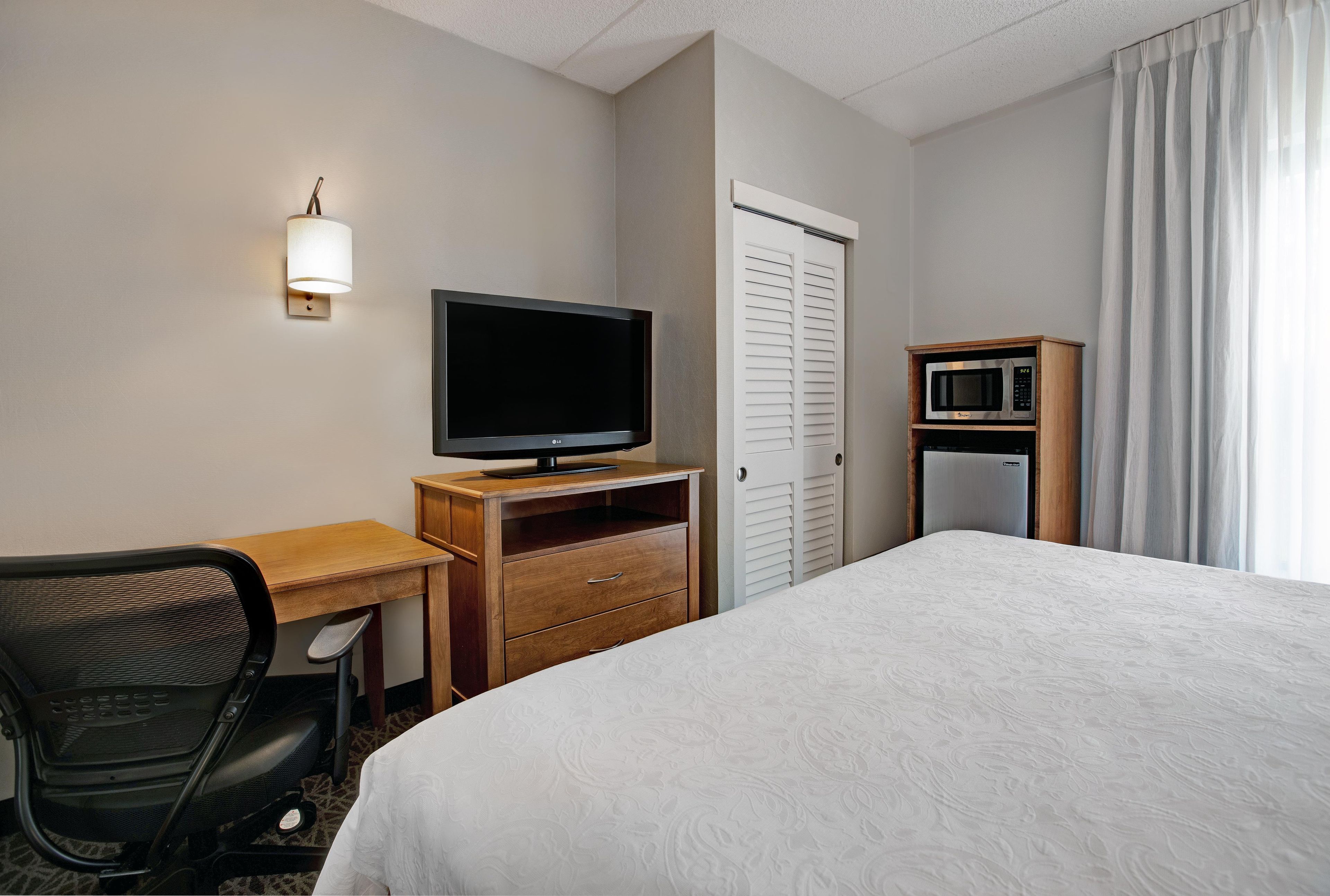 A hotel room with a bed, a desk with a chair, a television, a microwave, and a wardrobe.