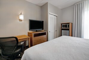 Quarto de hotel com cama, escrivaninha, cadeira, televisão, micro-ondas e guarda-roupa.