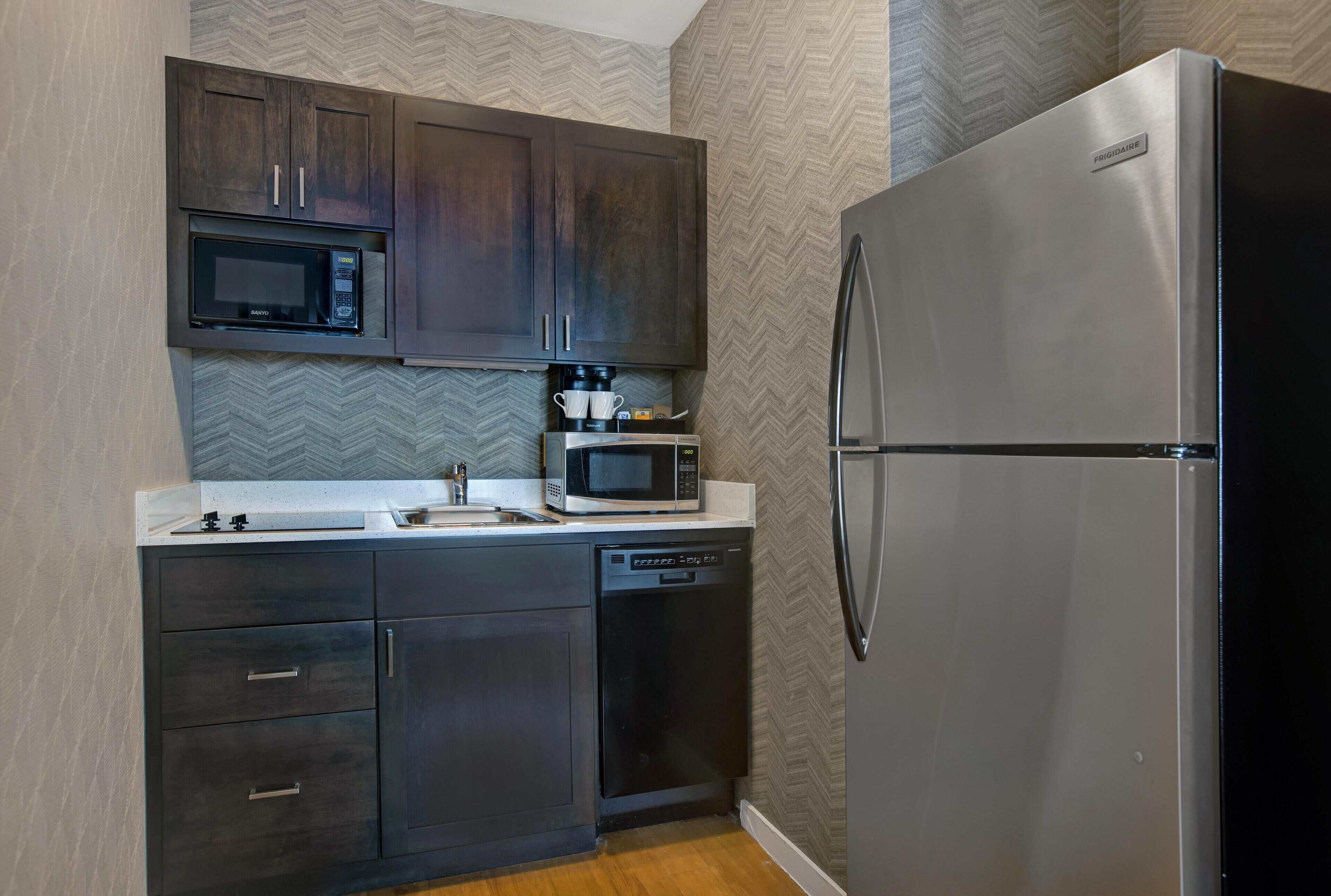 A compact kitchen with dark wooden cabinets, a stainless steel refrigerator, a microwave, and a dishwasher.
