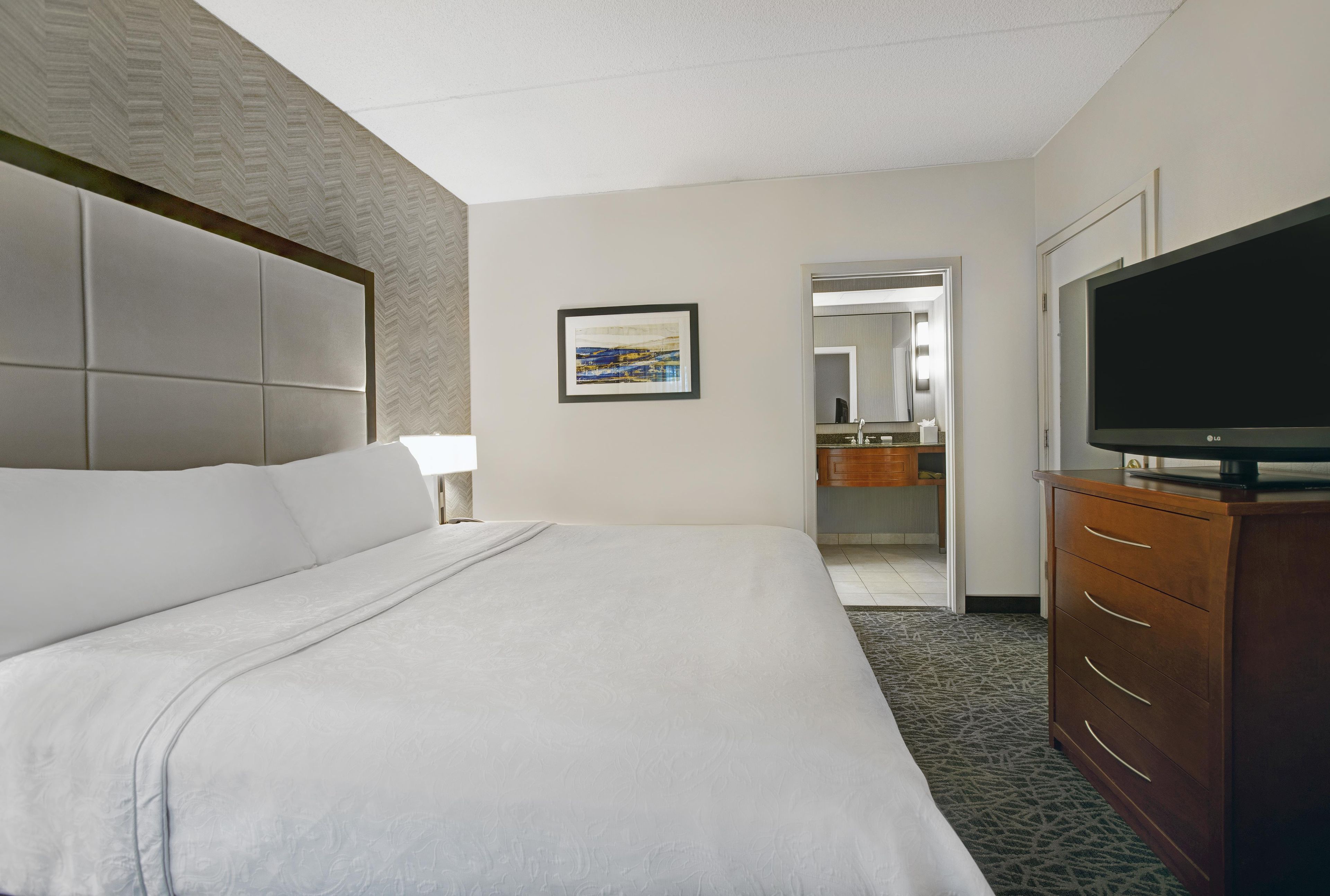 A hotel room with a large bed, a television on a wooden dresser, and a bathroom visible through an open door.