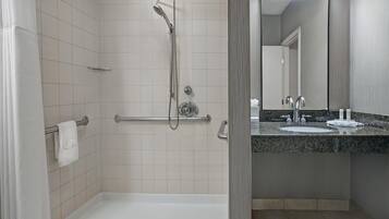 A modern bathroom with a walk-in shower, grab bars, a bathtub, and a granite countertop with a sink and mirror.