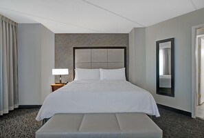 Ein Hotelzimmer mit einem großen Bett, einem Nachttisch mit Lampe, einer Bank, einem Spiegel und einem gemusterten Teppich.
