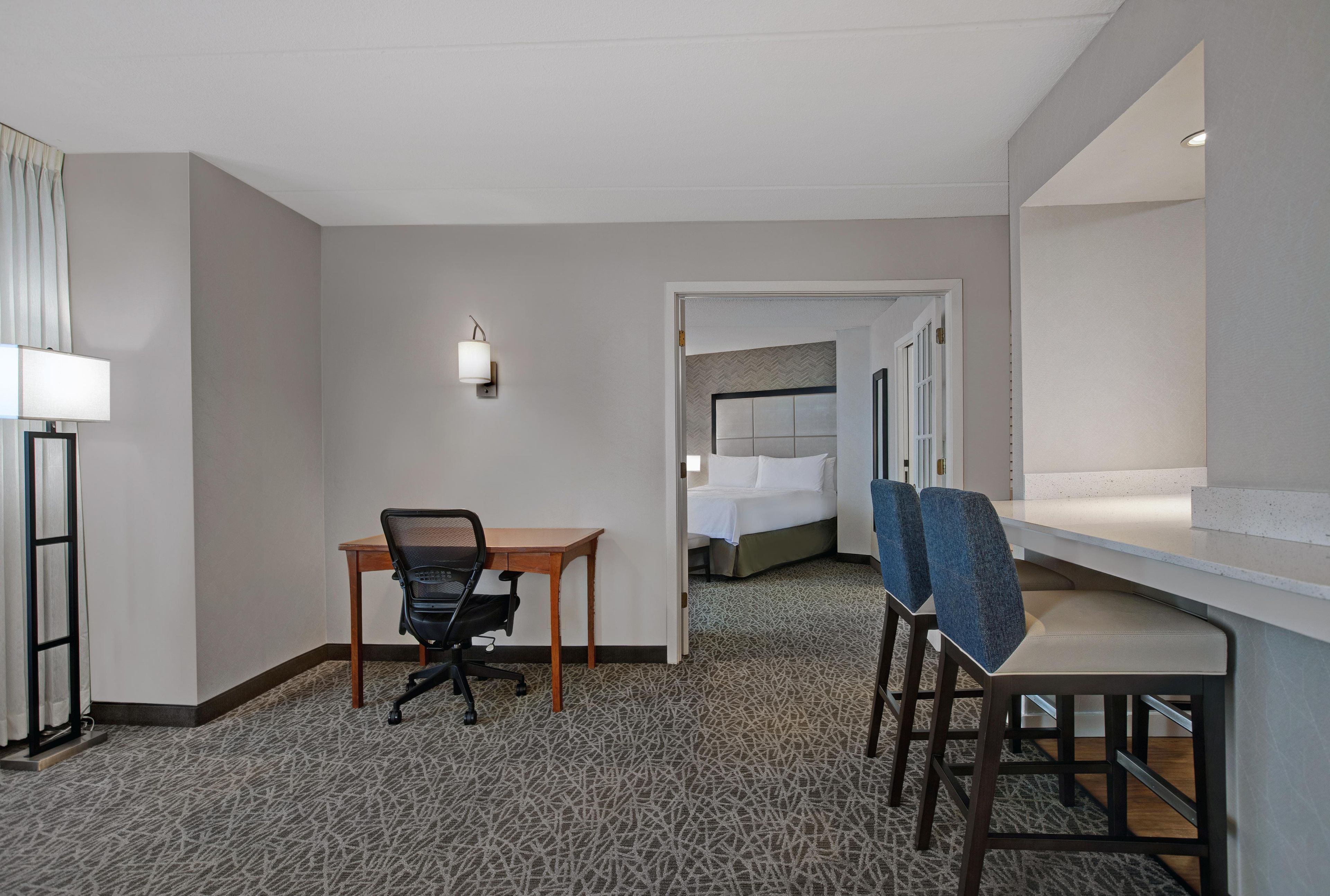 A hotel room with a desk, office chair, two chairs, a bed, and a nightstand.
