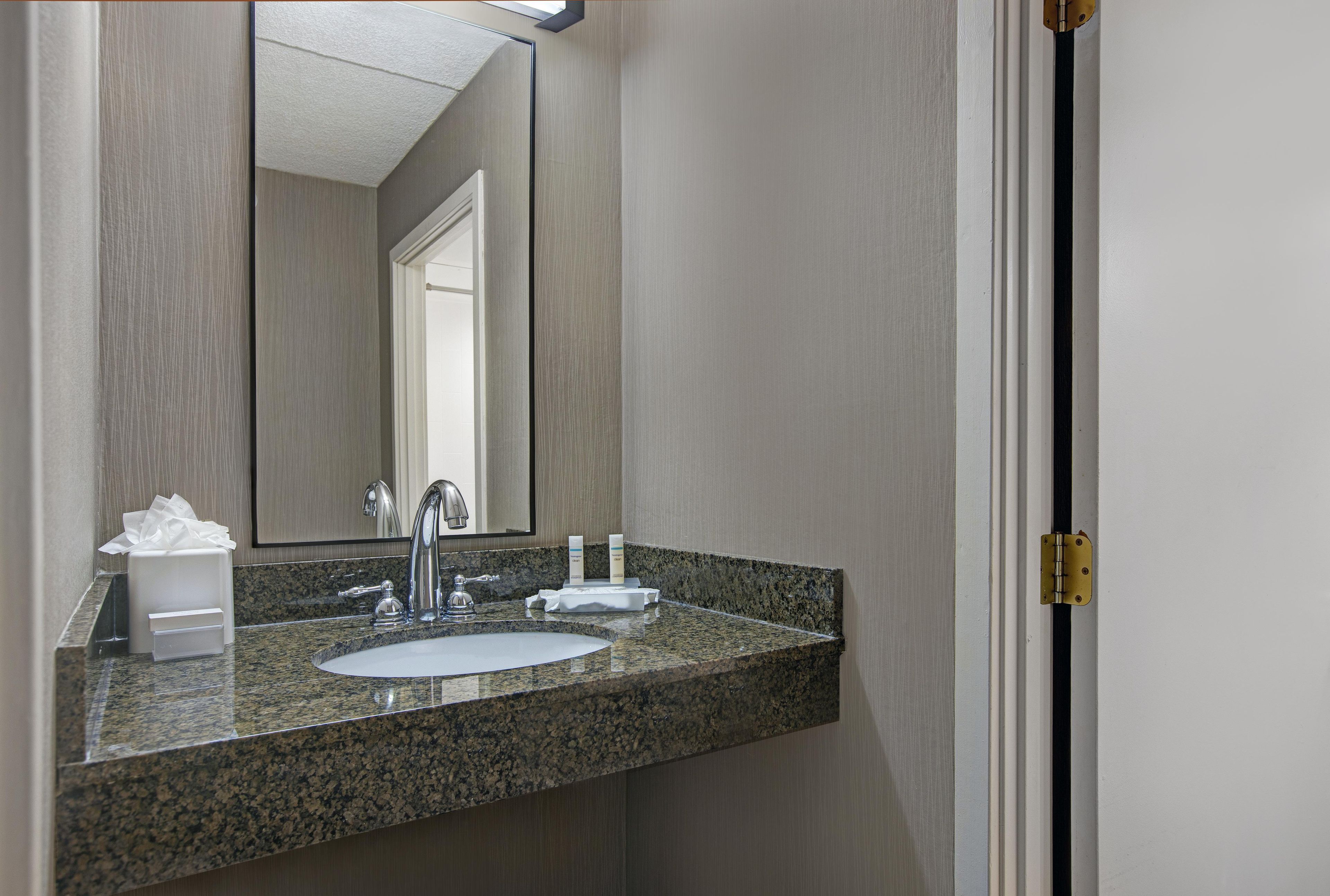Une salle de bain avec un comptoir en granit, un lavabo, un miroir et une porte.