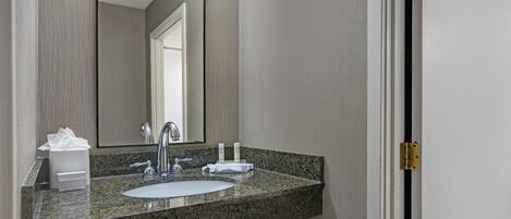 A bathroom with a granite countertop, a sink, a mirror, and a door.