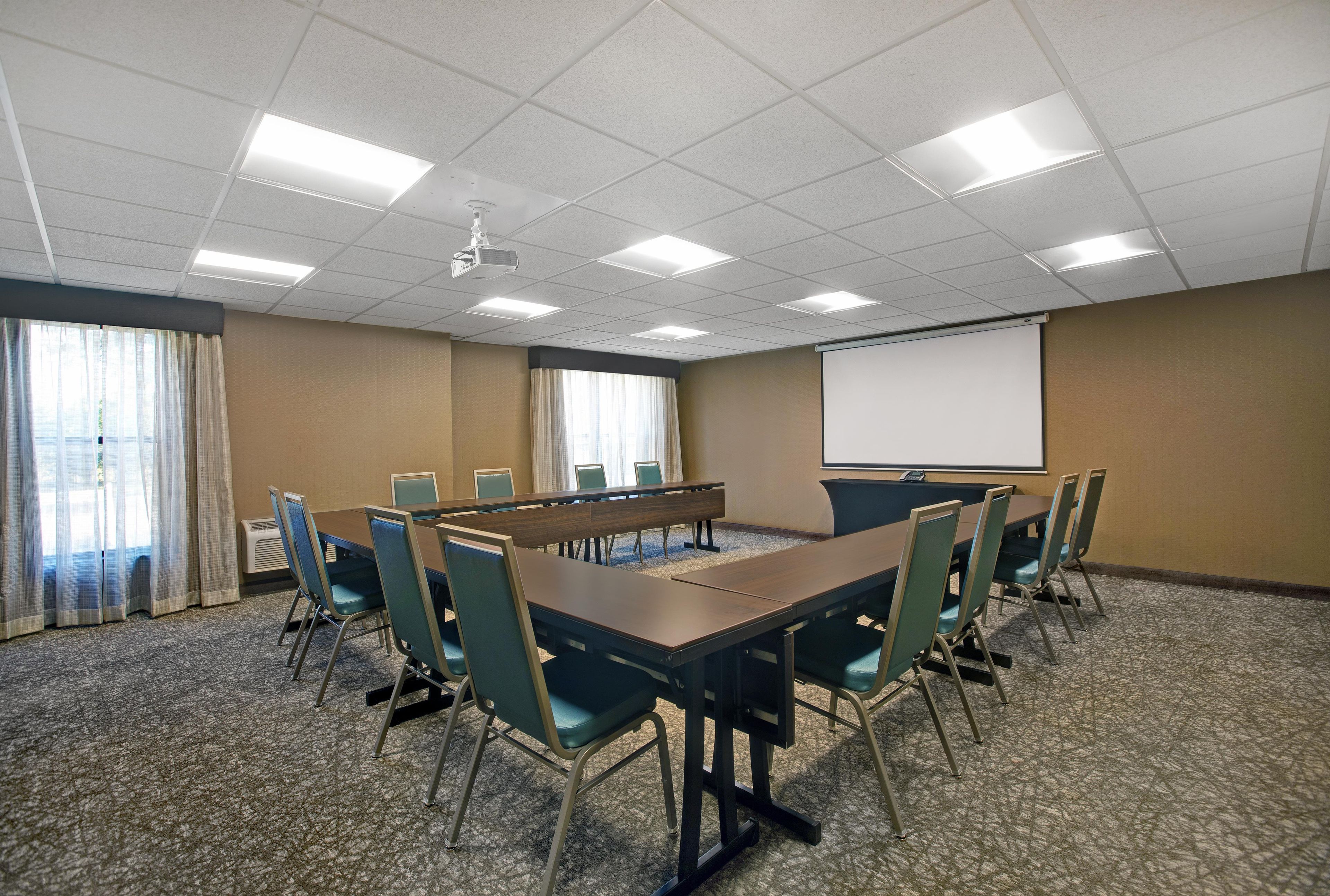 A conference room with a long table, chairs, a projector screen, and a large window with curtains.