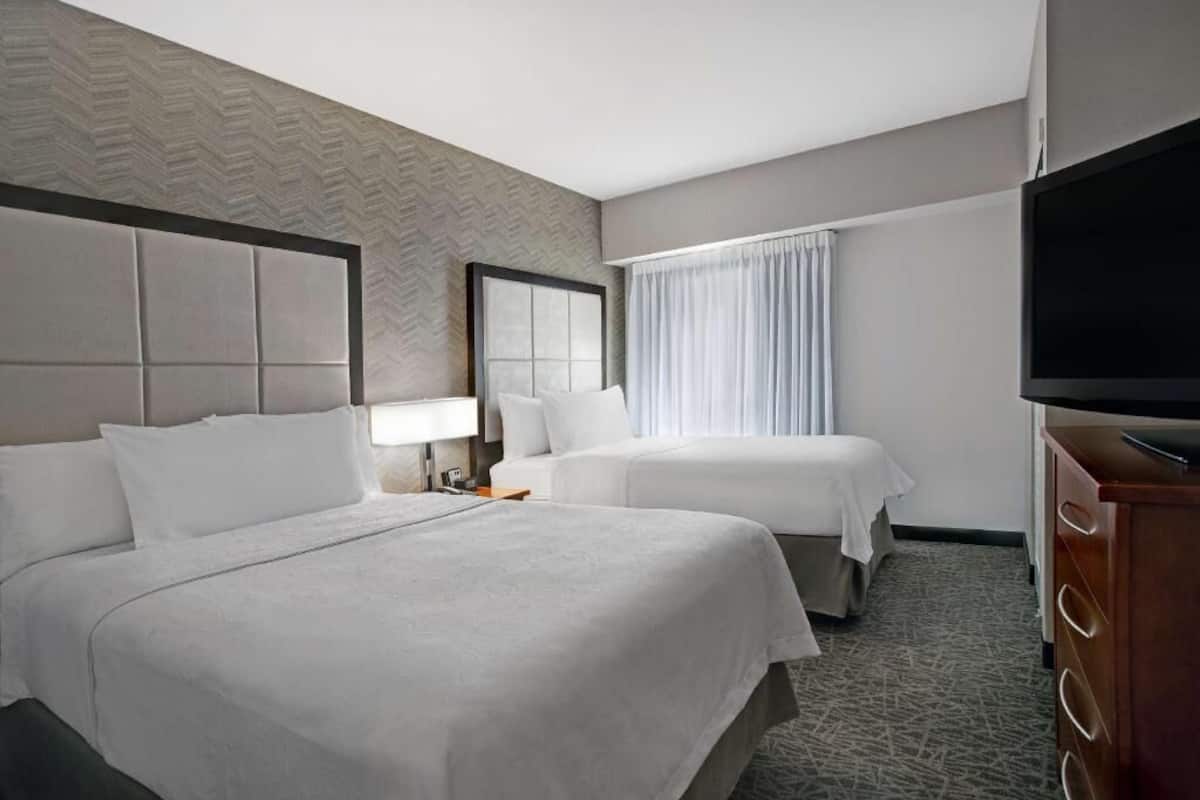 Een hotelkamer met twee bedden, een flatscreen televisie, een dressoir en een raam met gordijnen.