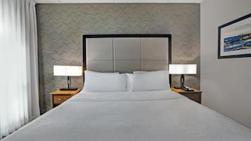 Un cuarto de hotel con una cama grande, dos mesitas de noche con lámparas, un papel tapiz con estampado de espiga y un cuadro en la pared.