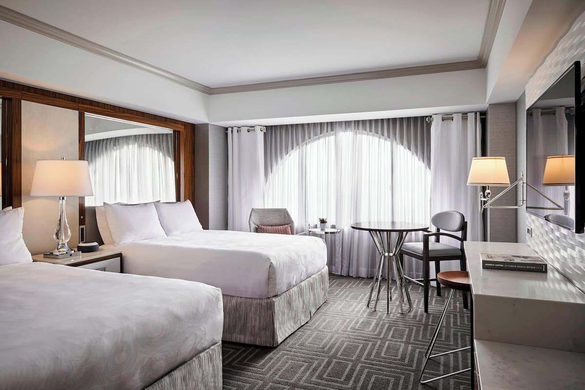 Habitación de hotel con dos camas, un escritorio, una silla, una mesita pequeña y un espejo grande.