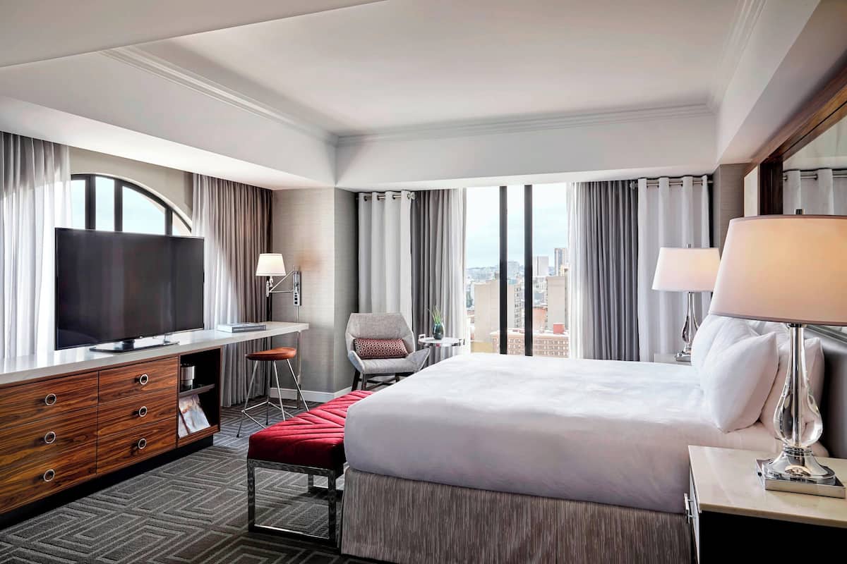 Habitación de hotel con una cama grande, televisión, escritorio con silla y vistas a la ciudad.