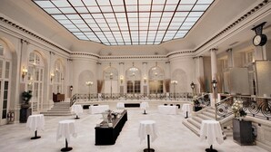 A grand hall with a high ceiling, arched windows, and a central table with chairs. - The Waldorf Hilton, London (London)