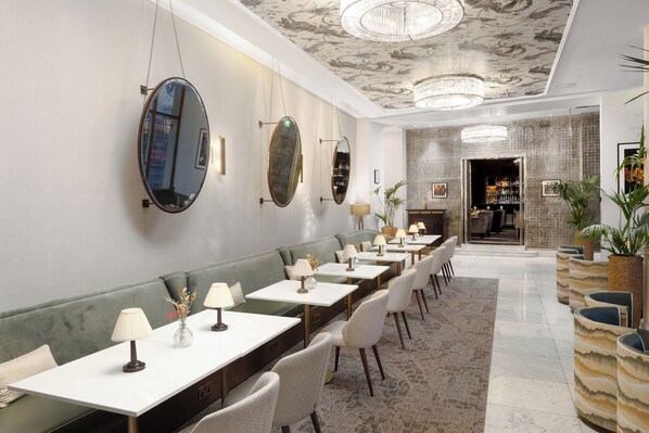 A long dining area with a green sofa, white tables, and chairs, and a bar in the background. - The Waldorf Hilton, London (London)