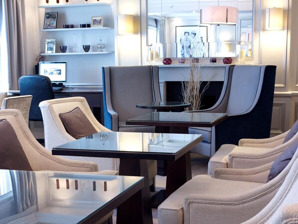 A modern living room with a glass coffee table, beige armchairs, and a dark-toned sofa.