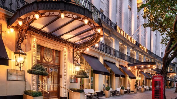 A hotel entrance with a classic facade, a red telephone booth, and outdoor seating. - The Waldorf Hilton, London (London)