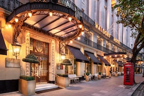 A hotel entrance with a classic facade, a red telephone booth, and outdoor seating.
