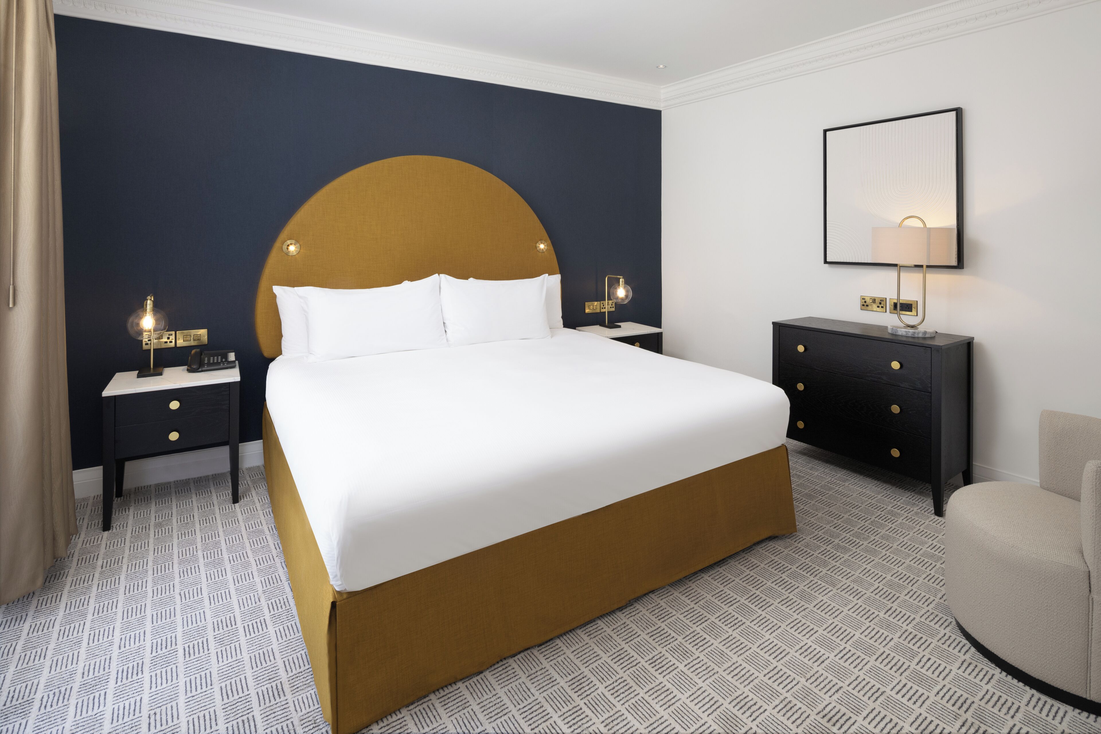 Una habitación de hotel con una cama grande, dos mesitas de noche, un tocador, un armario y una lámpara de pared.