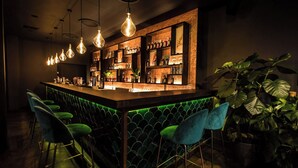 A bar area with a counter, green bar stools, hanging light fixtures, and shelves with bottles and decorations. - The Waldorf Hilton, London (London)