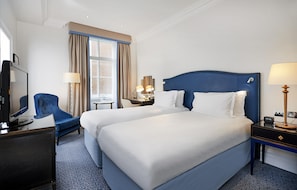 Habitación de hotel con dos camas, un escritorio, una silla, un televisor y una ventana con cortinas.