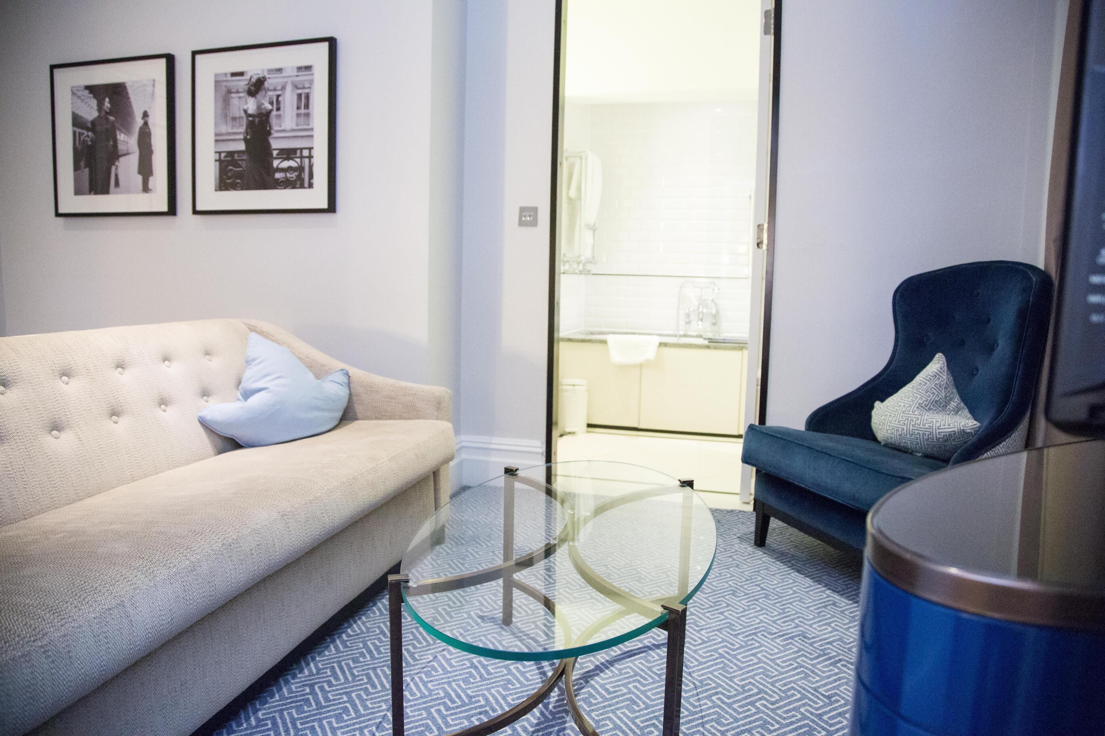 A living room with a sofa, a glass coffee table, a blue armchair, and a blue trash can.