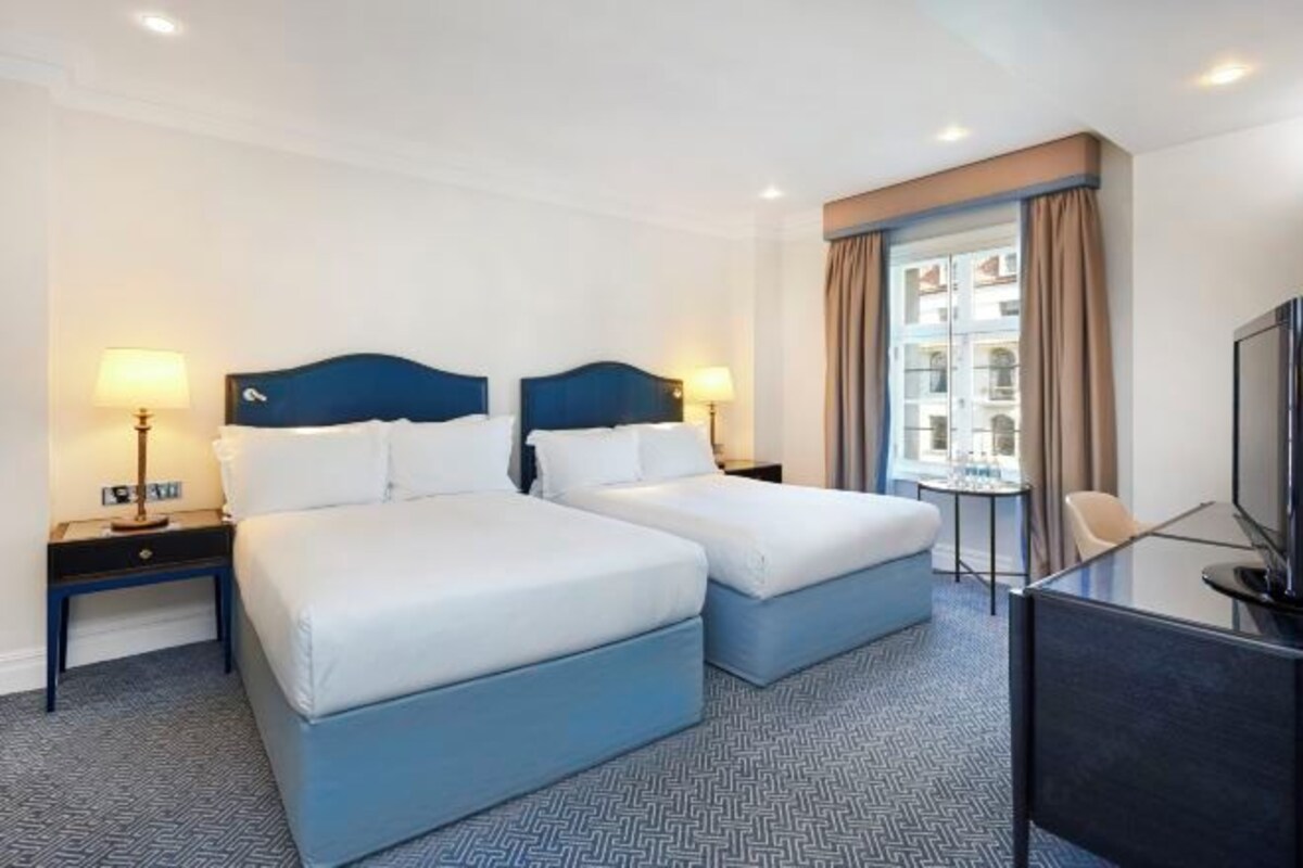 A hotel room with two beds, a desk, a television, and a window with curtains.