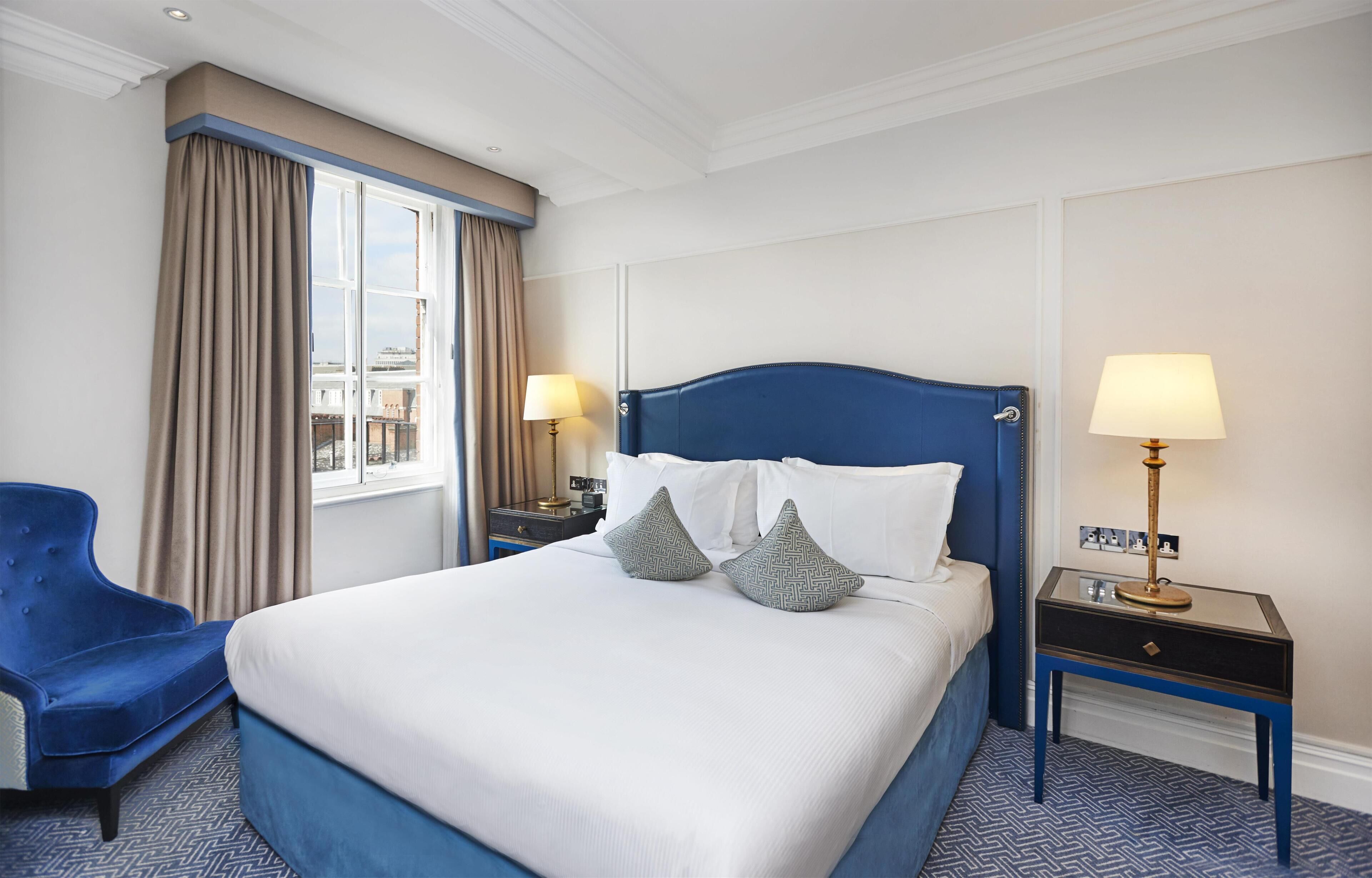 A hotel room with a large bed, two bedside tables, a chair, a window with curtains, and a city view.