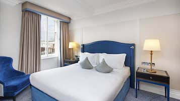 A hotel room with a large bed, two bedside tables, a chair, a window with curtains, and a city view.