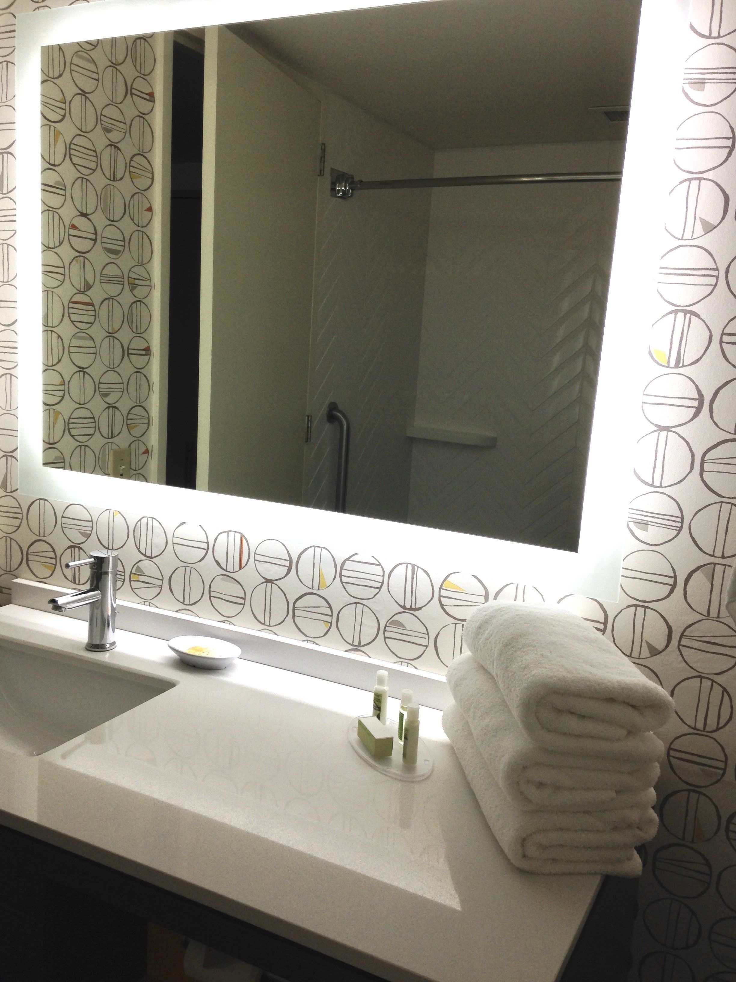 Une salle de bain avec un grand miroir, un lavabo et un porte-serviettes.