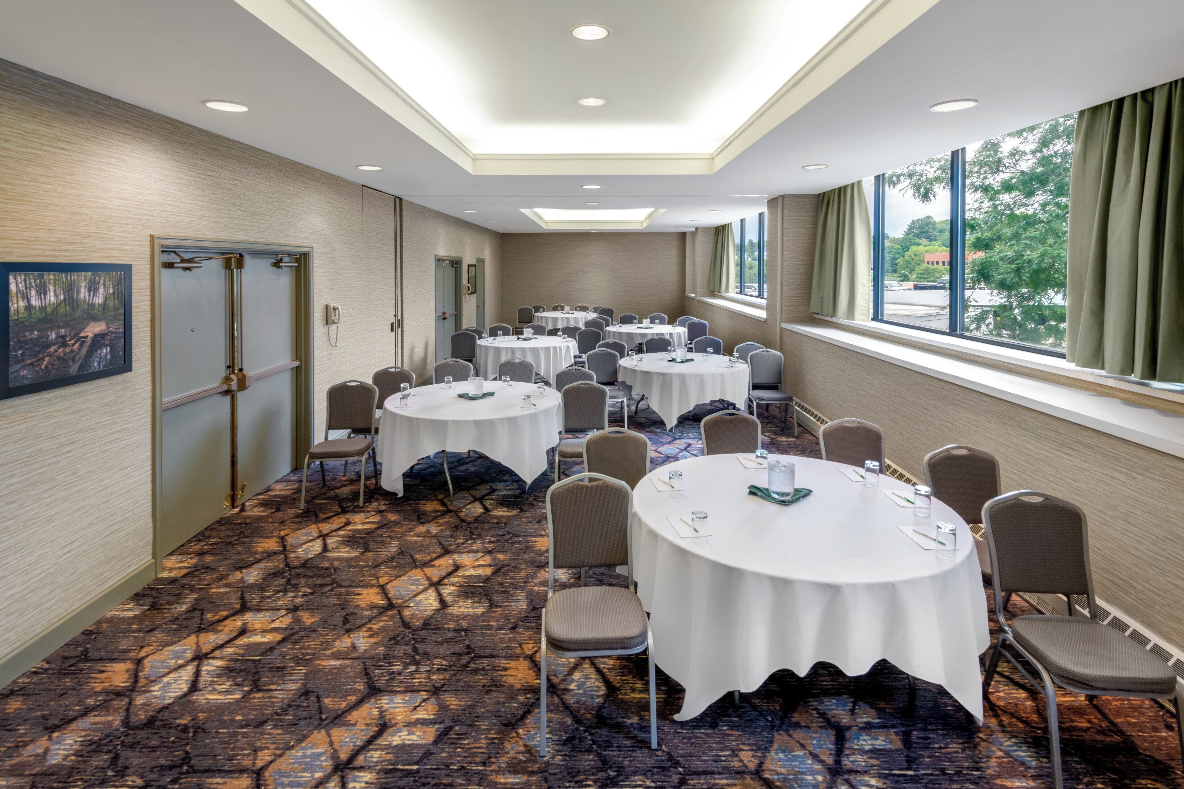 A conference room with multiple round tables, chairs, and a patterned carpet.