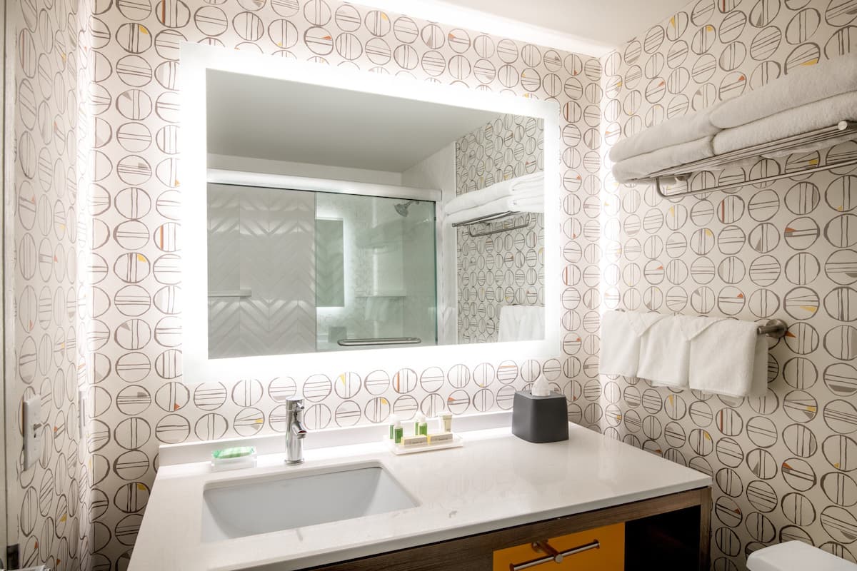 A bathroom with a large mirror, a sink, and a towel rack.