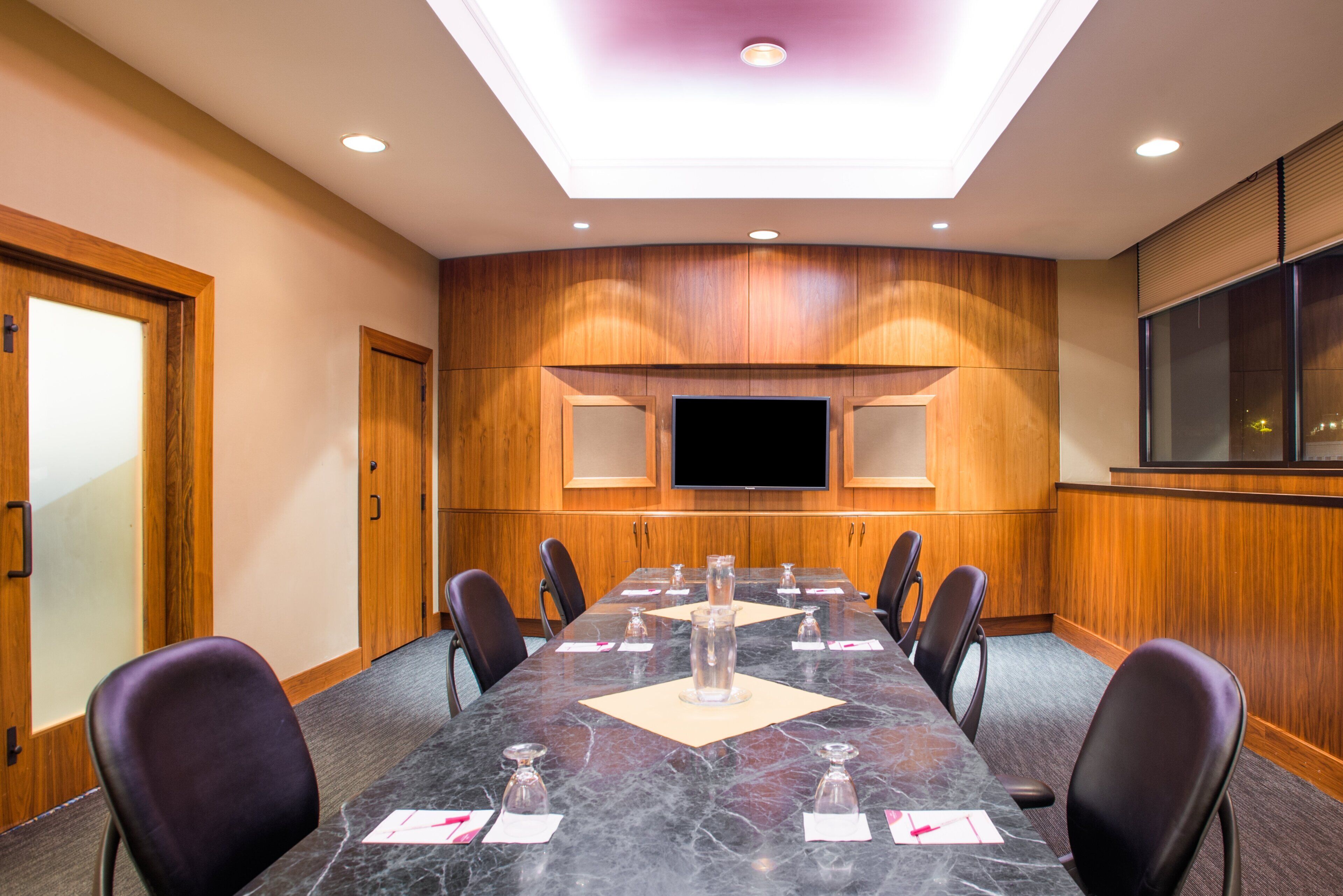 A conference room with a long table, chairs, a flat-screen TV, and wooden paneling on the walls.