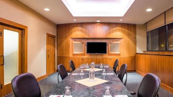 A conference room with a long table, chairs, a flat-screen TV, and wooden paneling on the walls.