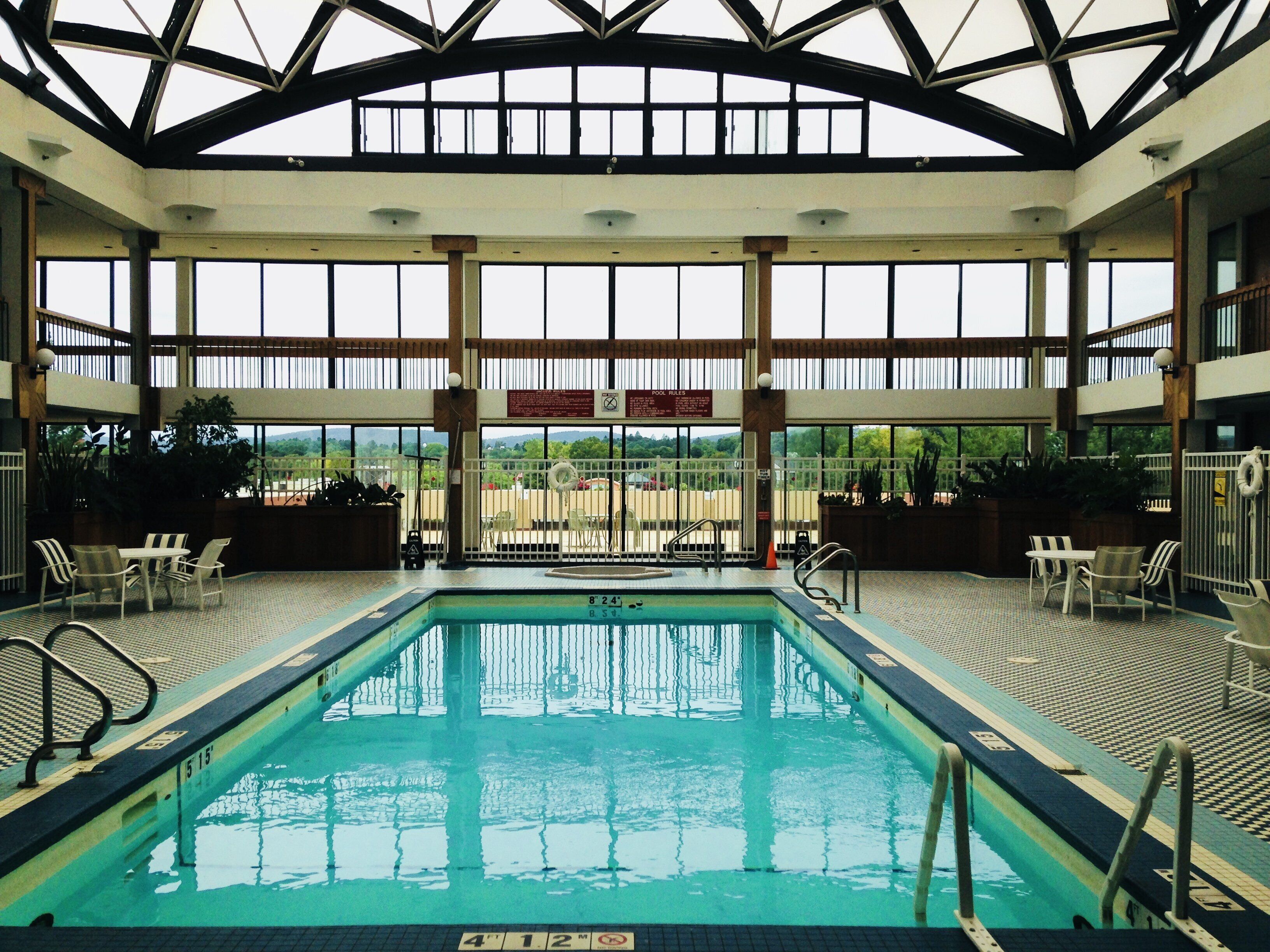 Une piscine intérieure avec des panneaux indiquant clairement les règles d’utilisation, plusieurs espaces de détente et une vue sur l’extérieur grâce à de grandes fenêtres.