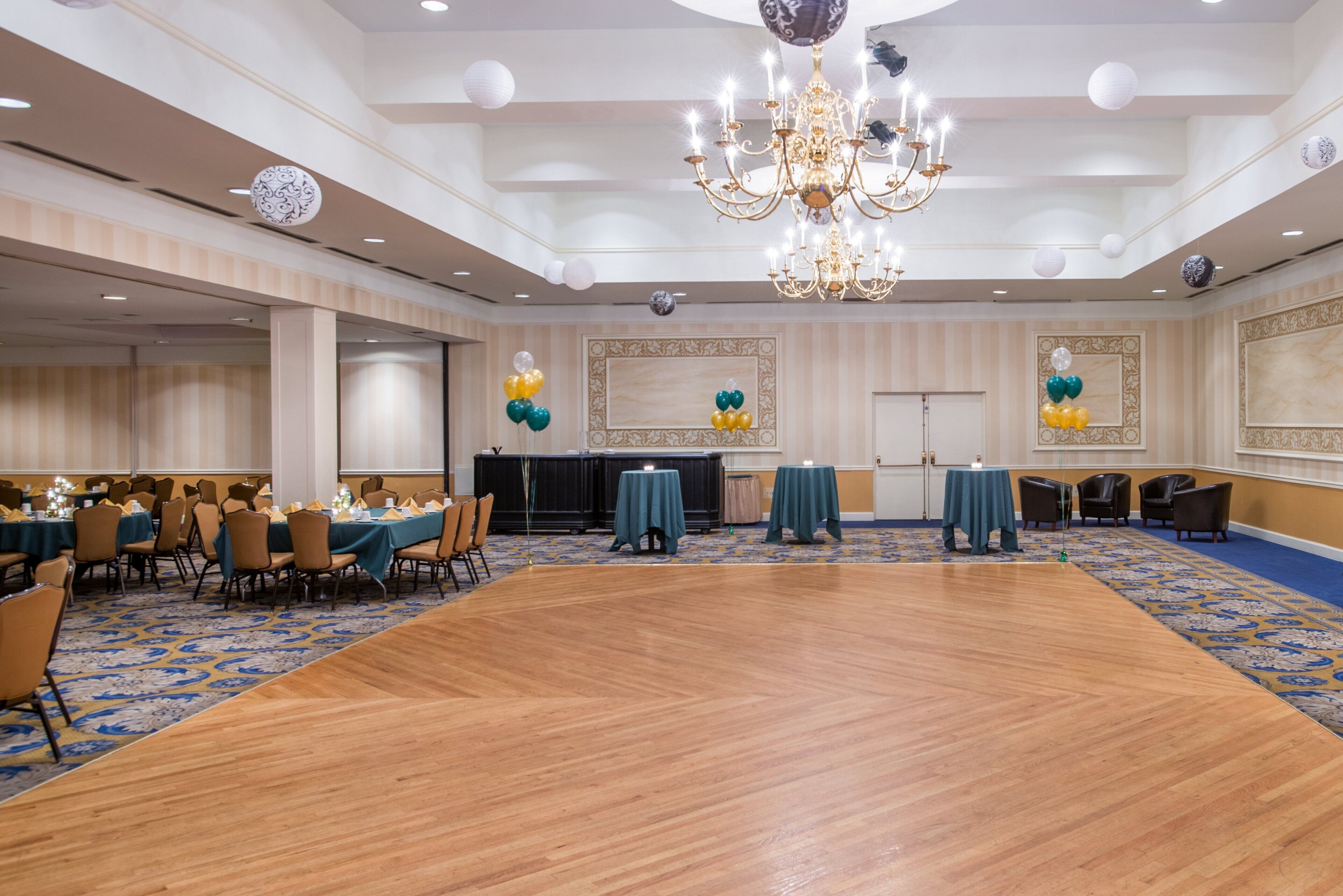 A spacious banquet hall with a large wooden floor, tables set for dining, and a grand chandelier.
